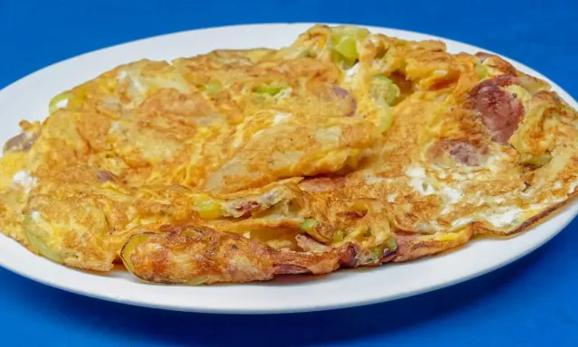 Złocisty omlet na słono z kawałkami kiełbasy i warzyw, podany na białym talerzu.