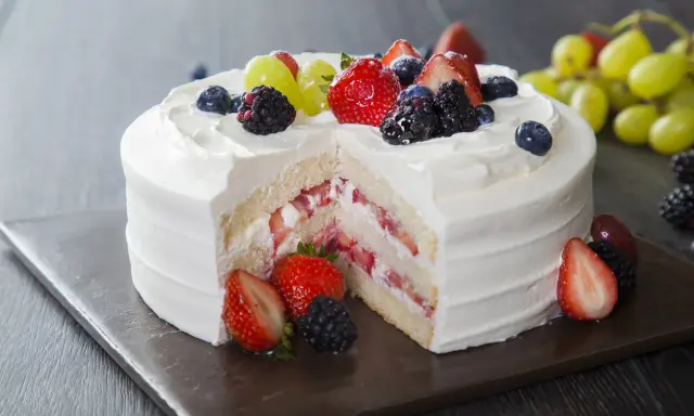 Pyszny tort z bitą śmietaną i serkiem mascarpone, przełożony świeżymi truskawkami i udekorowany owocami leśnymi.
