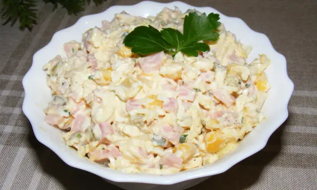 Pyszna sałatka na Wielkanoc z szynką, jajkiem i kukurydzą, udekorowana natką pietruszki.