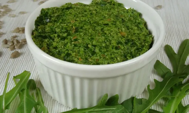 Domowe pesto z rukoli, pełne świeżości i aromatu, w białej miseczce. Obok świeże liście rukoli i nasiona słonecznika.