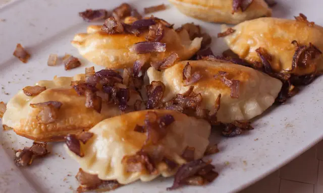 Pyszne pierogi z mięsem, okraszone chrupiącą cebulką, kuszą na białym talerzu.
