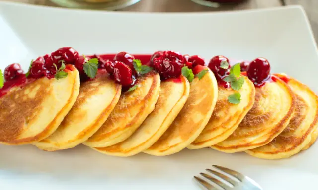 Puszyste pancakes na maślance, polane wiśniowym sosem i ozdobione listkami mięty. Idealne na słodkie śniadanie.
