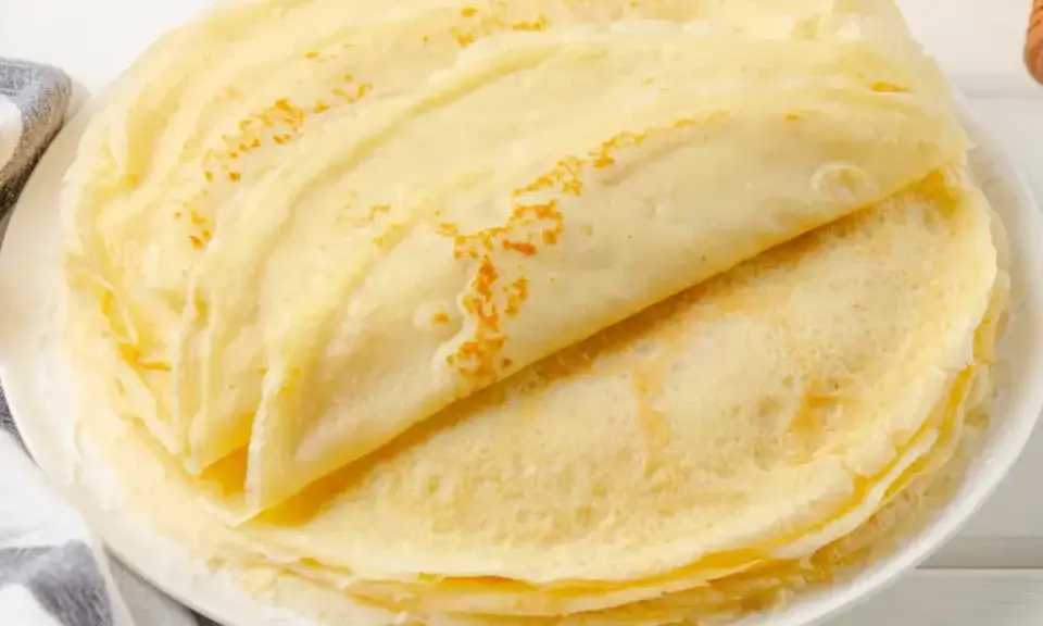 Stos cienkich, złotych naleśników bez jajek, ułożonych na białym talerzu. Idealne na śniadanie lub deser.