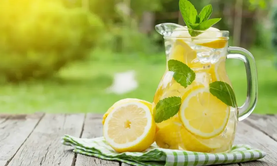 Jak zrobić dobrą lemoniadę? Orzeźwiający dzbanek z cytrynami, lodem i miętą na drewnianym stole w ogrodzie.