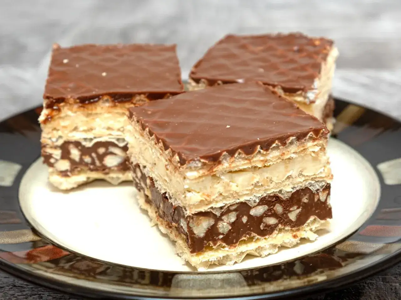 Trzy kawałki czekoladowych wafli z kremem i orzechami, przypominające domowe wafle z mlekiem w proszku.