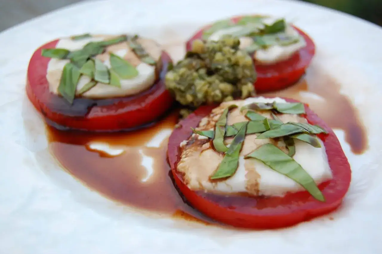 Sałatka Caprese z pomidor&oacute;w, mozzarelli i świeżej bazylii, podana z aromatycznym pesto z bazylii.