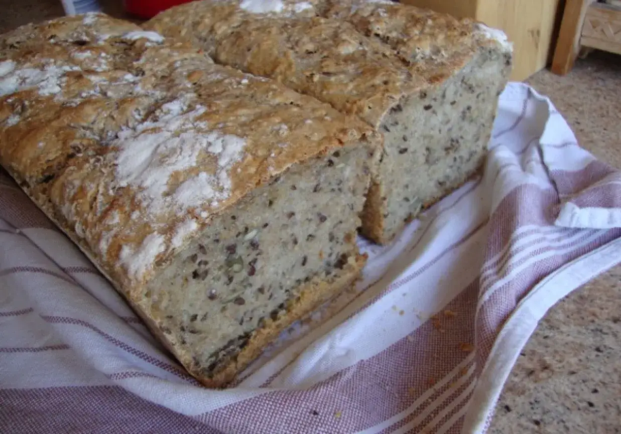 Dwa bochenki pysznego, domowego chleba na zakwasie, z widocznymi ziarnami, leżą na lnianej ściereczce.