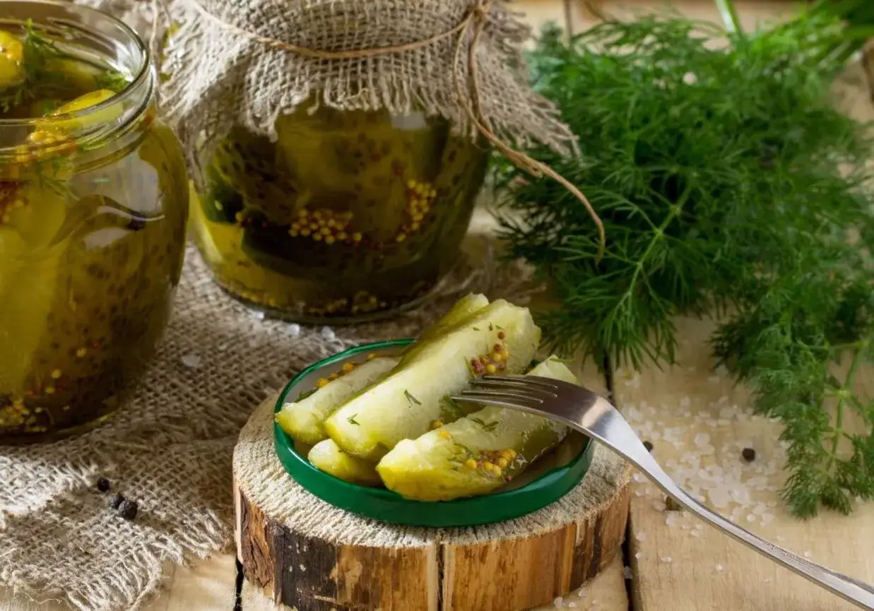 Słoiki z og&oacute;rkami w musztardzie, świeży koperek i widelec z kawałkami og&oacute;rka.