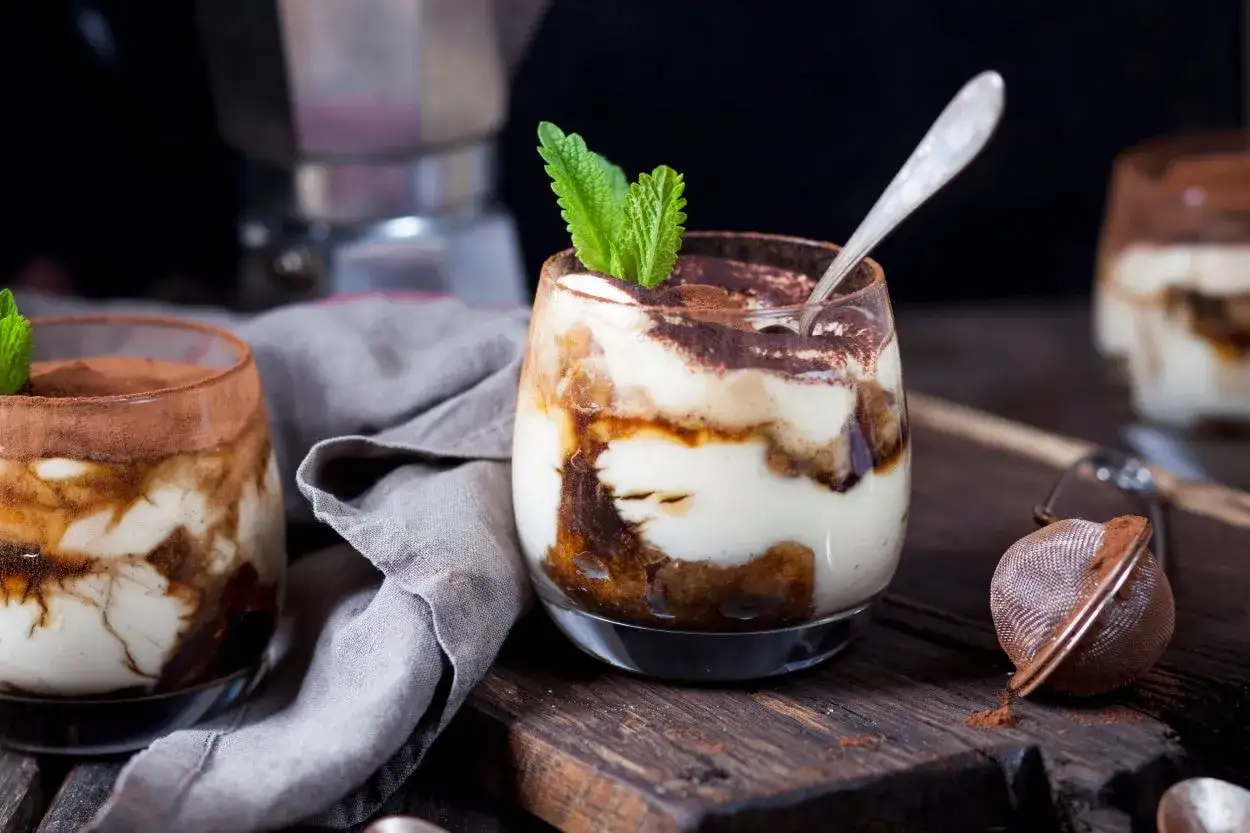 Pyszne tiramisu w pucharkach, udekorowane listkiem mięty, czeka na spr&oacute;bowanie.