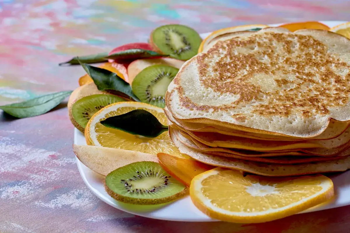 Stos puszystych naleśnik&oacute;w z budyniem, udekorowany plasterkami kiwi, pomarańczy i jabłka.