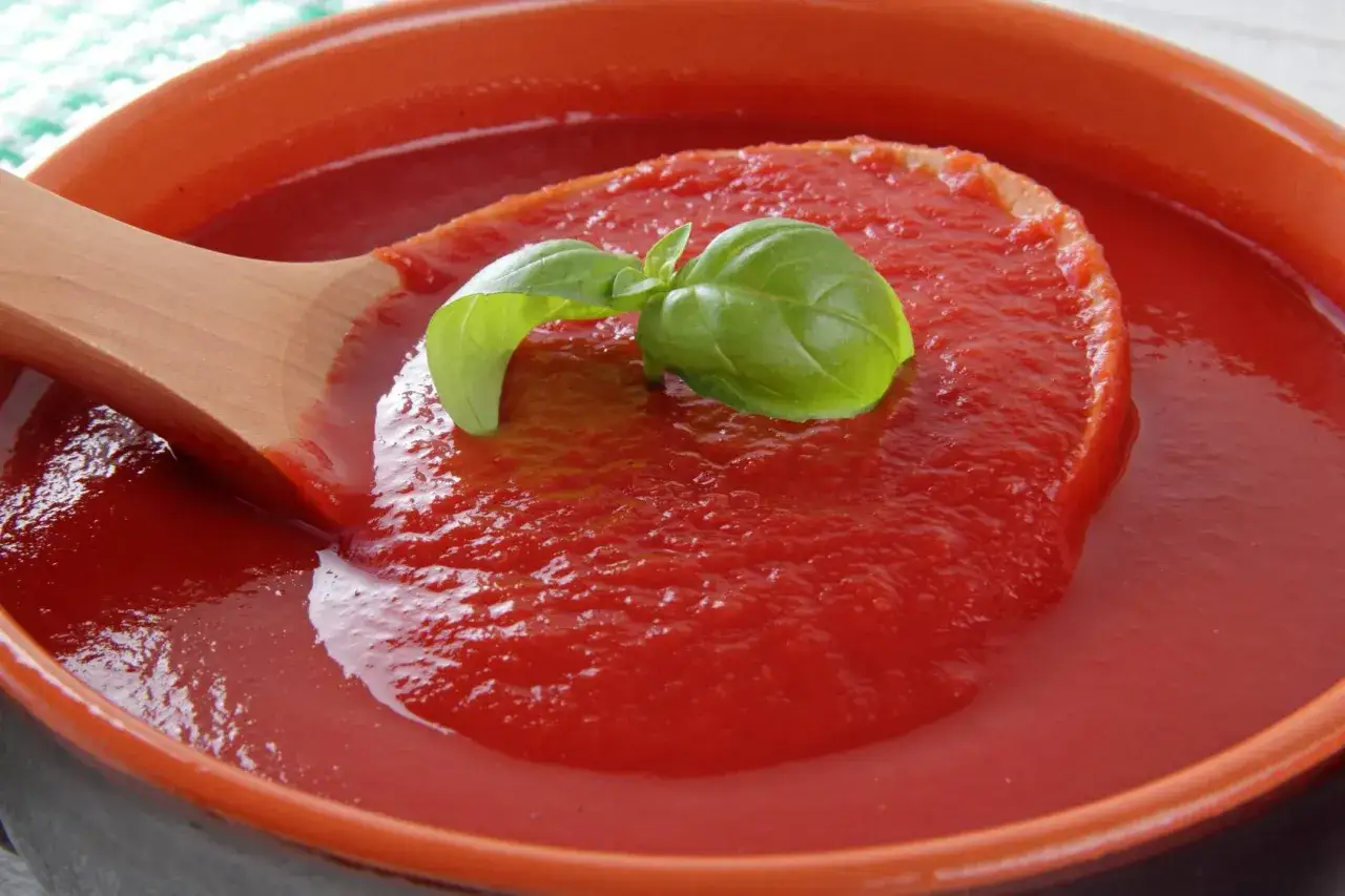 Gęsty, domowy ketchup z pomidor&oacute;w, nabierany drewnianą łyżką, ozdobiony listkiem bazylii. Idealny przepis na lato!