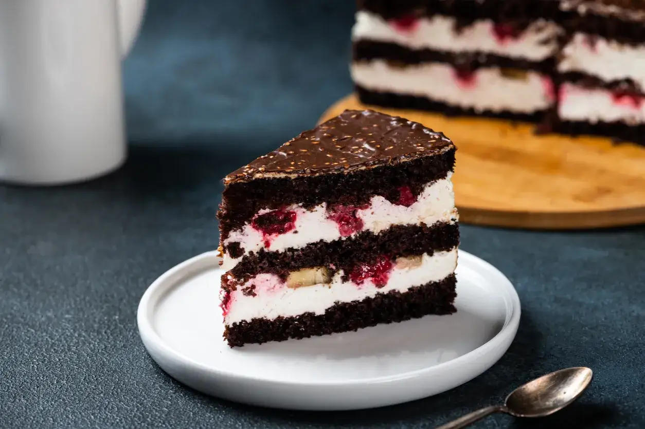 Pyszny tort z bitą śmietaną i serkiem mascarpone, przełożony malinami i bananami, oblany czekoladą.