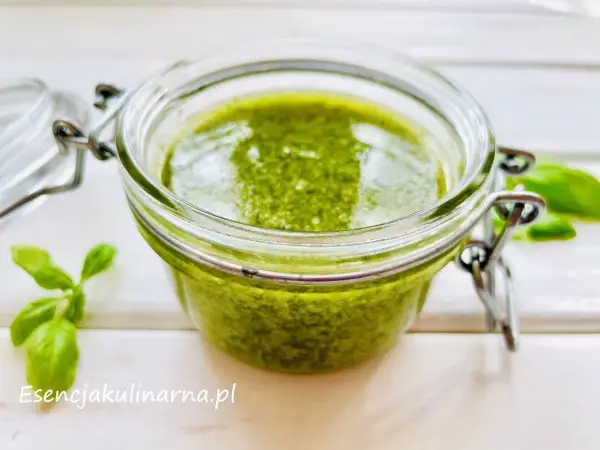 Słoiczek pełen aromatycznego pesto z bazylii, obok świeże listki. Idealne do makaronu i kanapek.